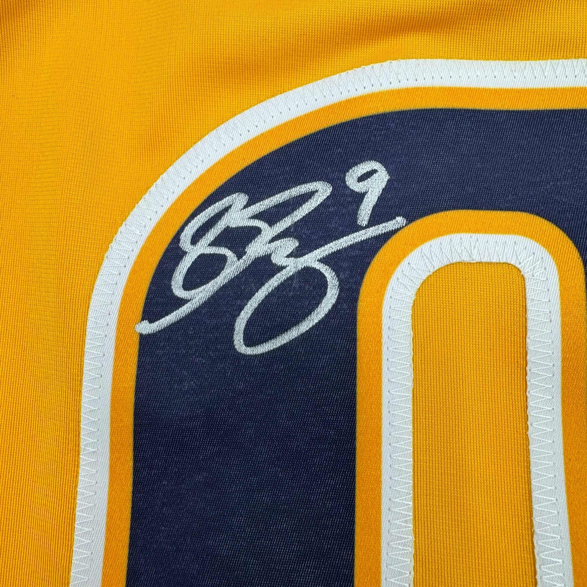 Close-up of Filip Forsberg's handwritten signature in silver ink on navy blue chest panel of yellow hockey jersey.