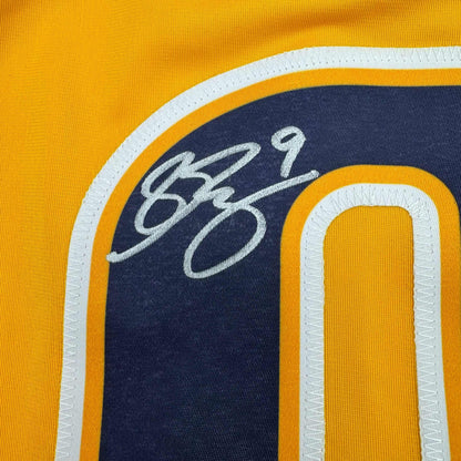 Close-up of Filip Forsberg's handwritten signature in silver ink on navy blue chest panel of yellow hockey jersey.