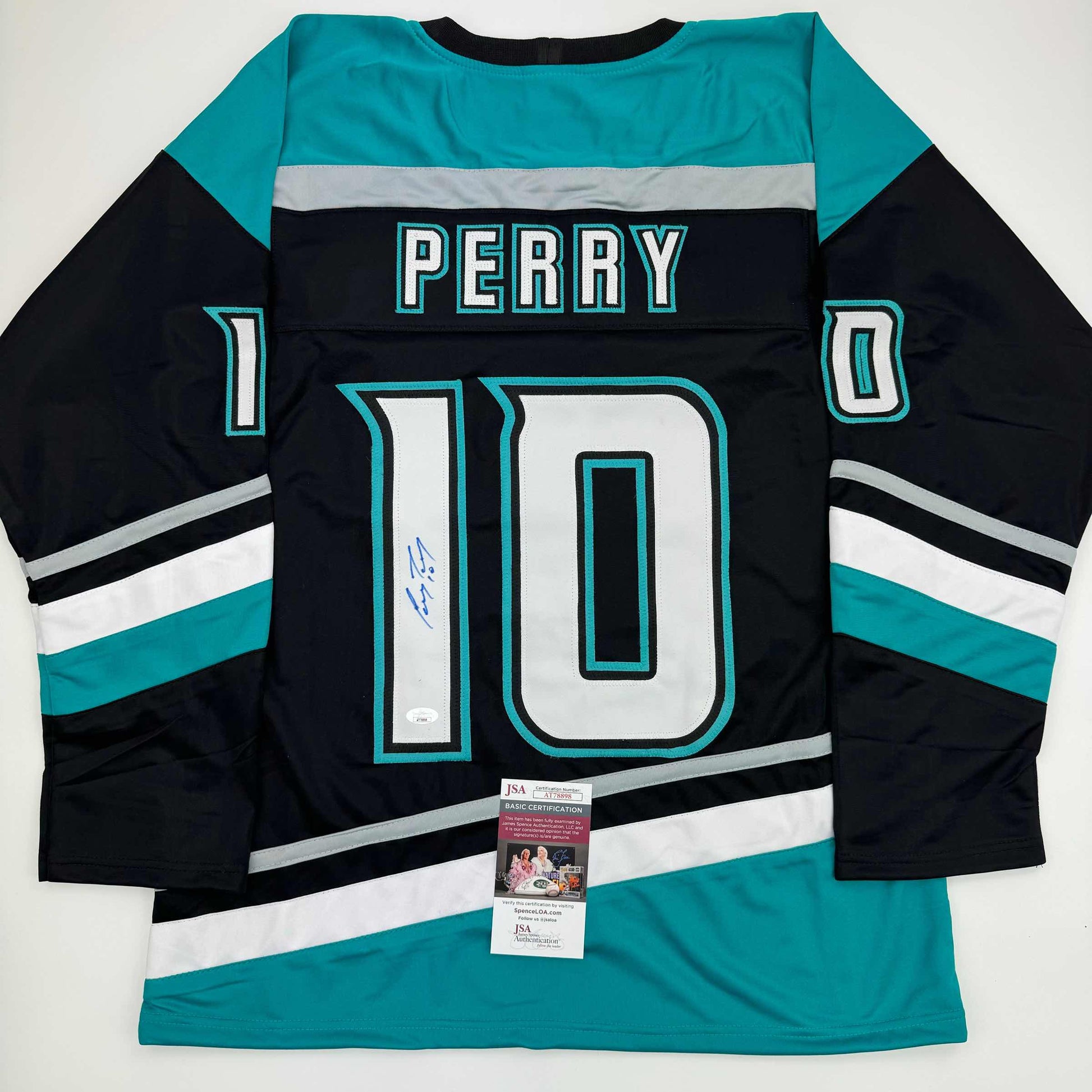 Black and teal hockey jersey number 10 with "PERRY" name plate, signed in blue ink, displayed flat with JSA authentication certificate visible at bottom.