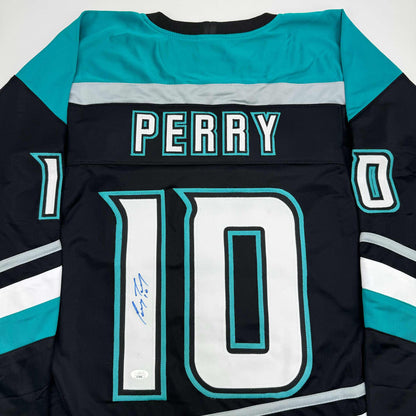 Flat lay of black, turquoise, and white hockey jersey displaying "PERRY" nameplate and number 10 with blue autograph on front.