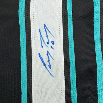 Close-up of blue handwritten signature on white stripe with turquoise and black striped hockey jersey fabric.