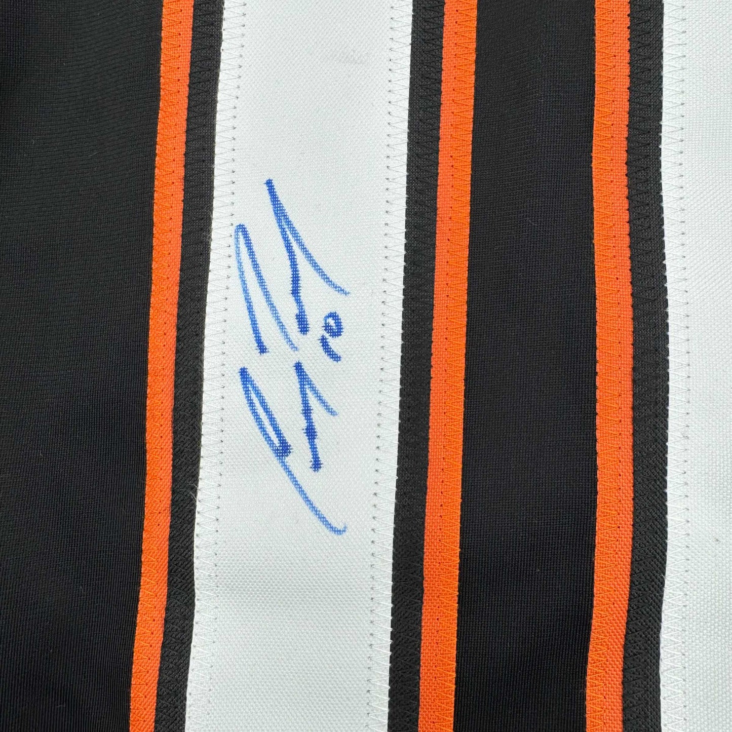 Close-up of blue handwritten signature on white stripe of black and orange striped hockey jersey.