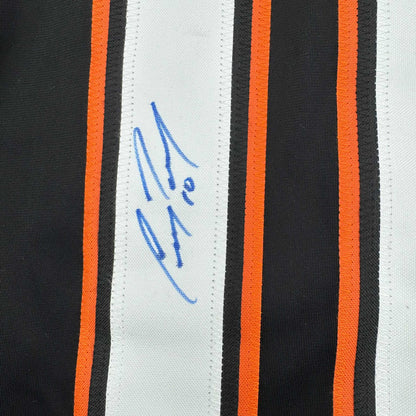 Close-up of blue handwritten signature on white stripe of black and orange striped hockey jersey.