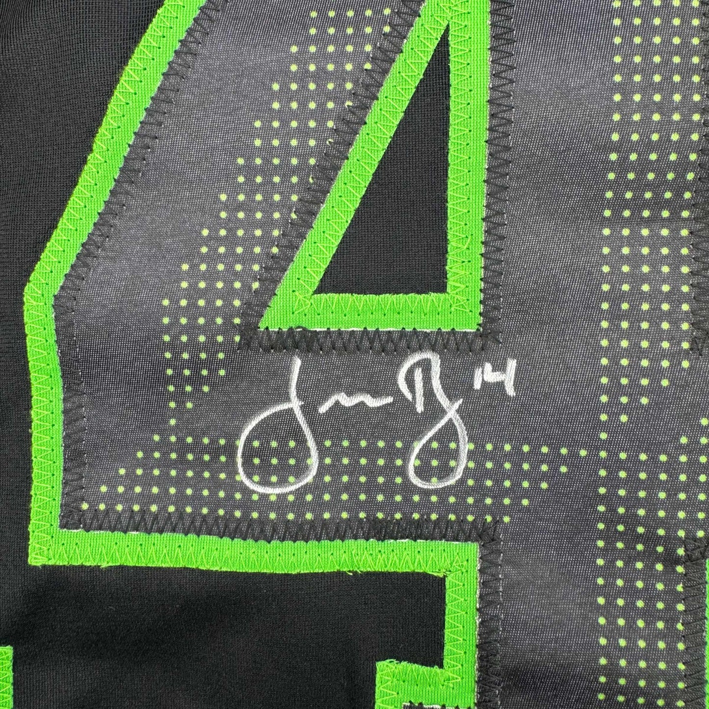 Close-up of neon green embroidered binding and mesh fabric detail on black hockey jersey with dotted pattern.