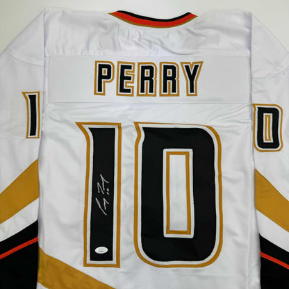 Back view of white hockey jersey with "PERRY" and number "10" in black and gold, displaying signature on number.