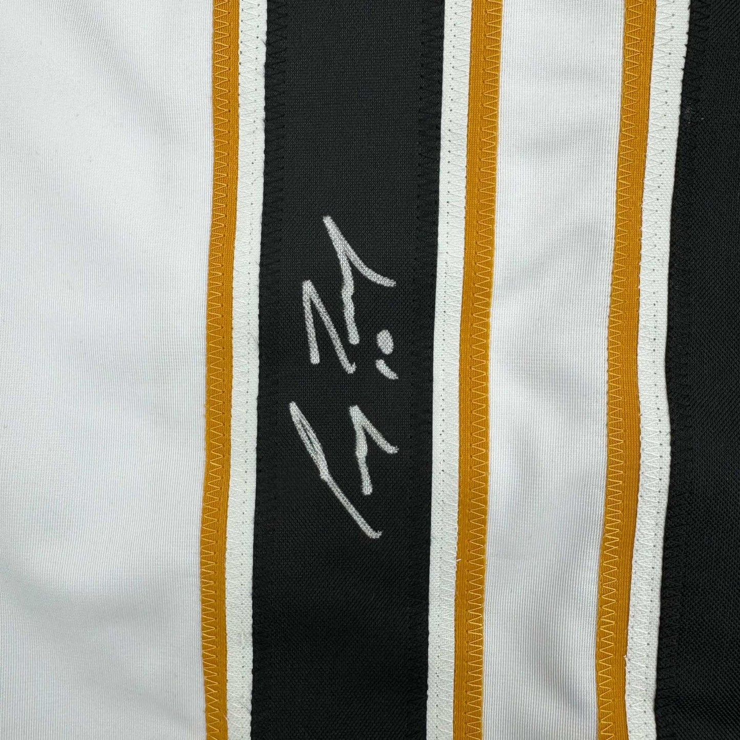 Close-up of autographed black stripe on white hockey jersey showing handwritten signature in silver ink.