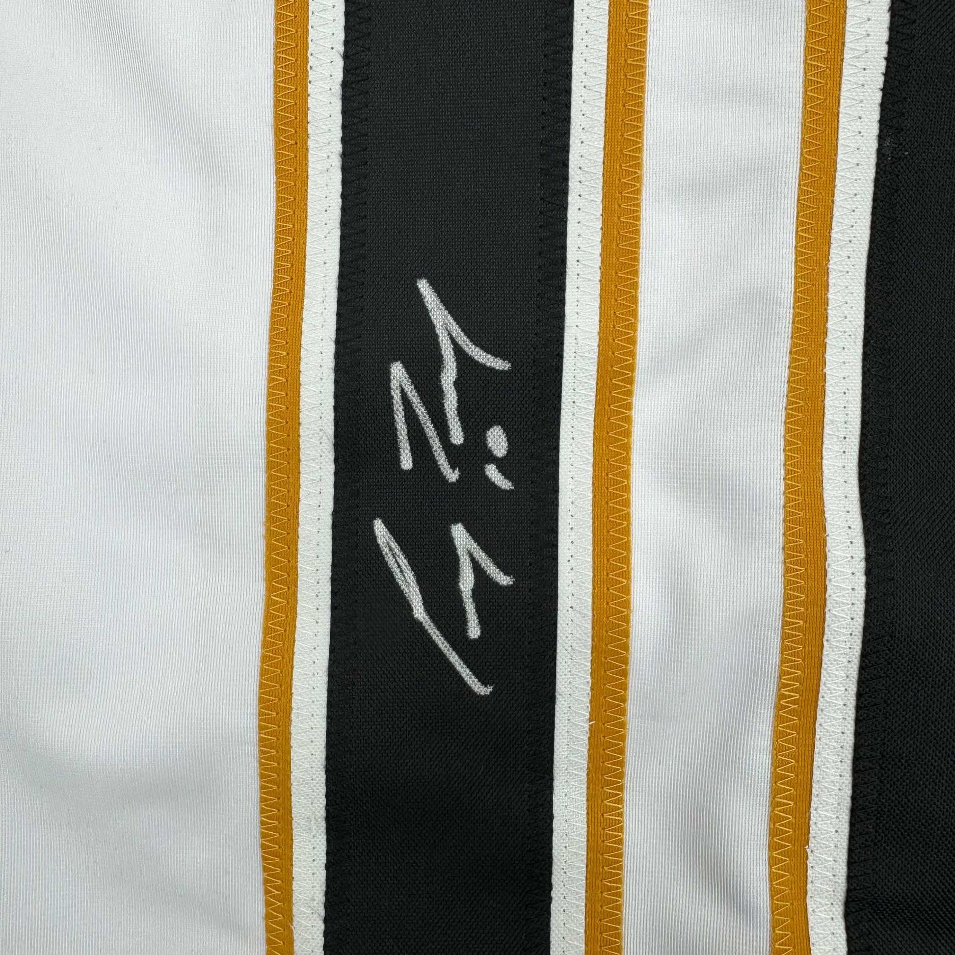 Close-up of autographed black stripe on white hockey jersey showing handwritten signature in silver ink.