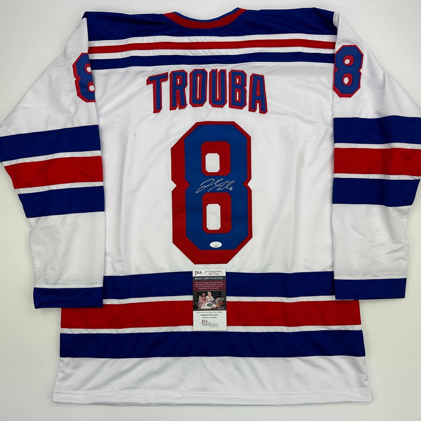 Back view of white hockey jersey with navy and red stripes, number 8, "TROUBA" nameplate, and JSA authentication certificate attached.