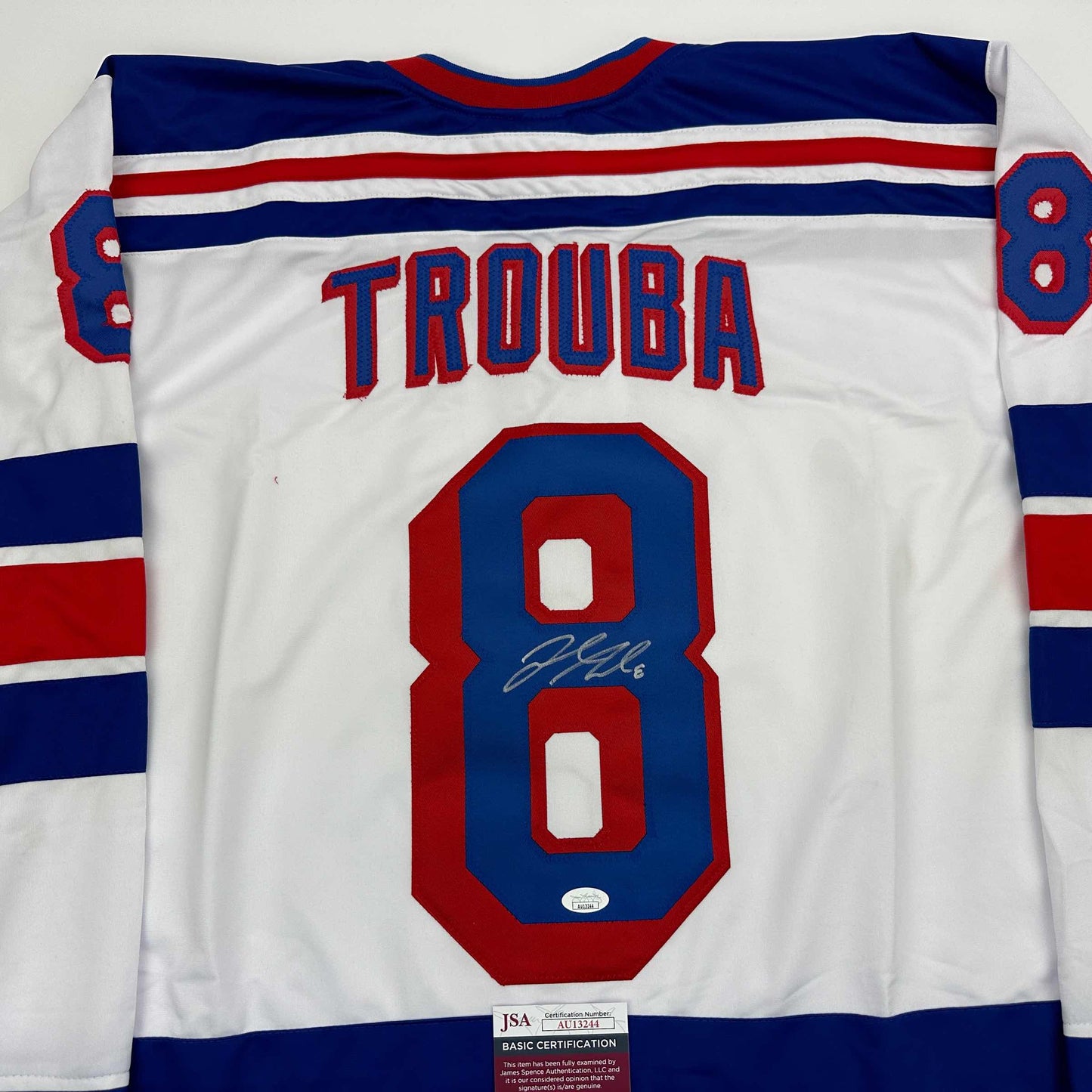 White hockey jersey with blue and red stripes displaying "TROUBA" and number 8, with visible autograph and JSA certification label.