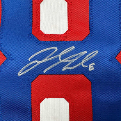 Close-up of signed blue and red hockey jersey chest area showing white cursive autograph on blue fabric.