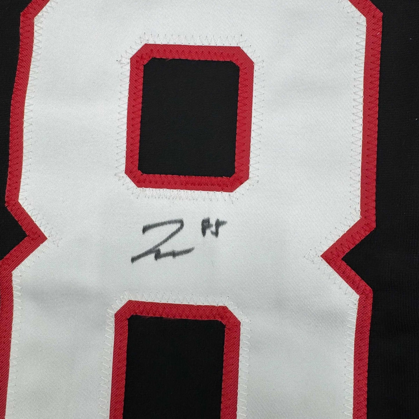 Close-up of white hockey jersey back with red trim and hand-signed "22 H" in black marker.