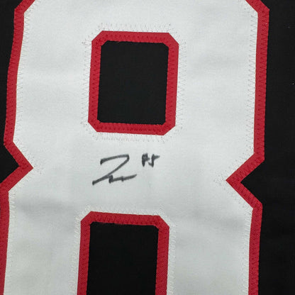 Close-up of white jersey back showing red-bordered number cutouts with handwritten signature below upper cutout.