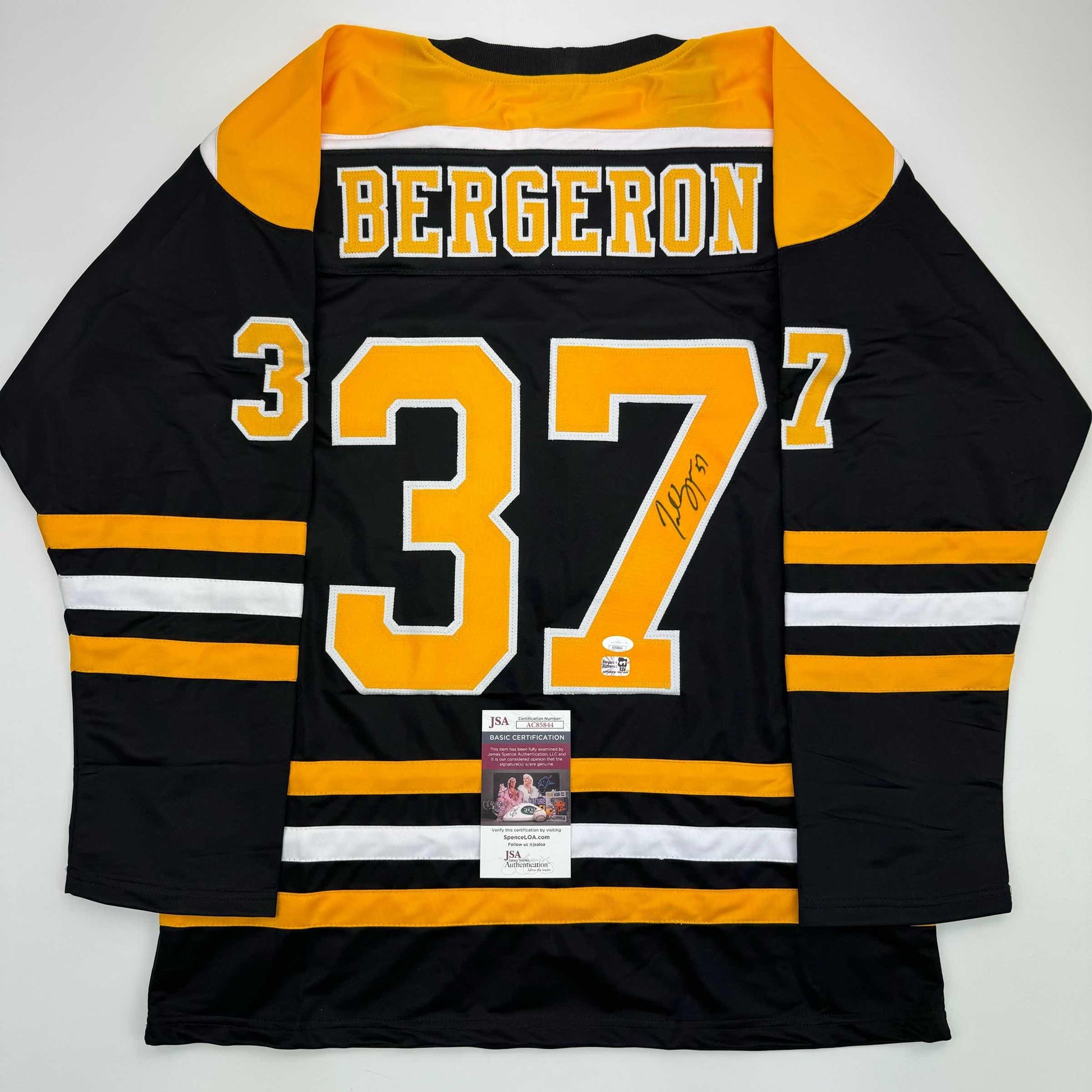 Black and gold Boston Bruins hockey jersey number 37 with "BERGERON" name and autograph, displayed flat with JSA authentication certificate visible.