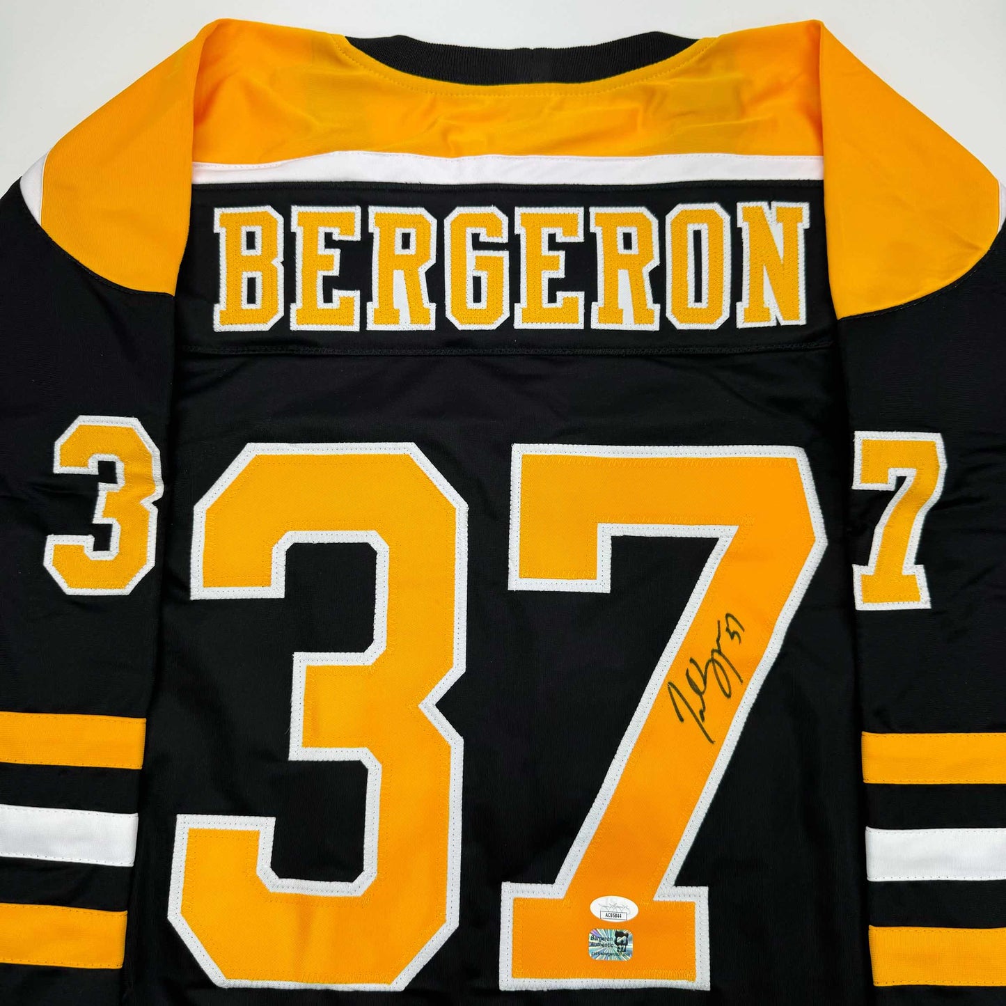 Flat lay of black Boston Bruins jersey with gold and white number 37, "BERGERON" nameplate, and handwritten signature on the orange number.