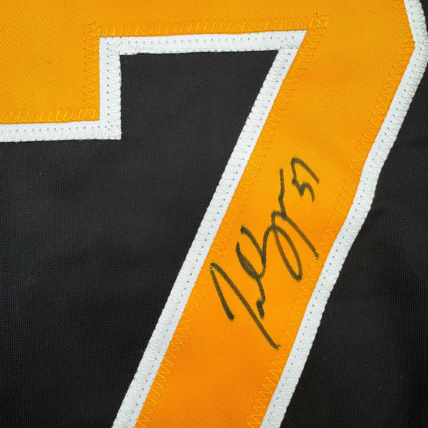 Close-up of signed black and gold hockey jersey stripe with handwritten autograph in dark ink.