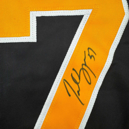 Close-up of signed black and gold hockey jersey stripe with handwritten autograph in dark ink.