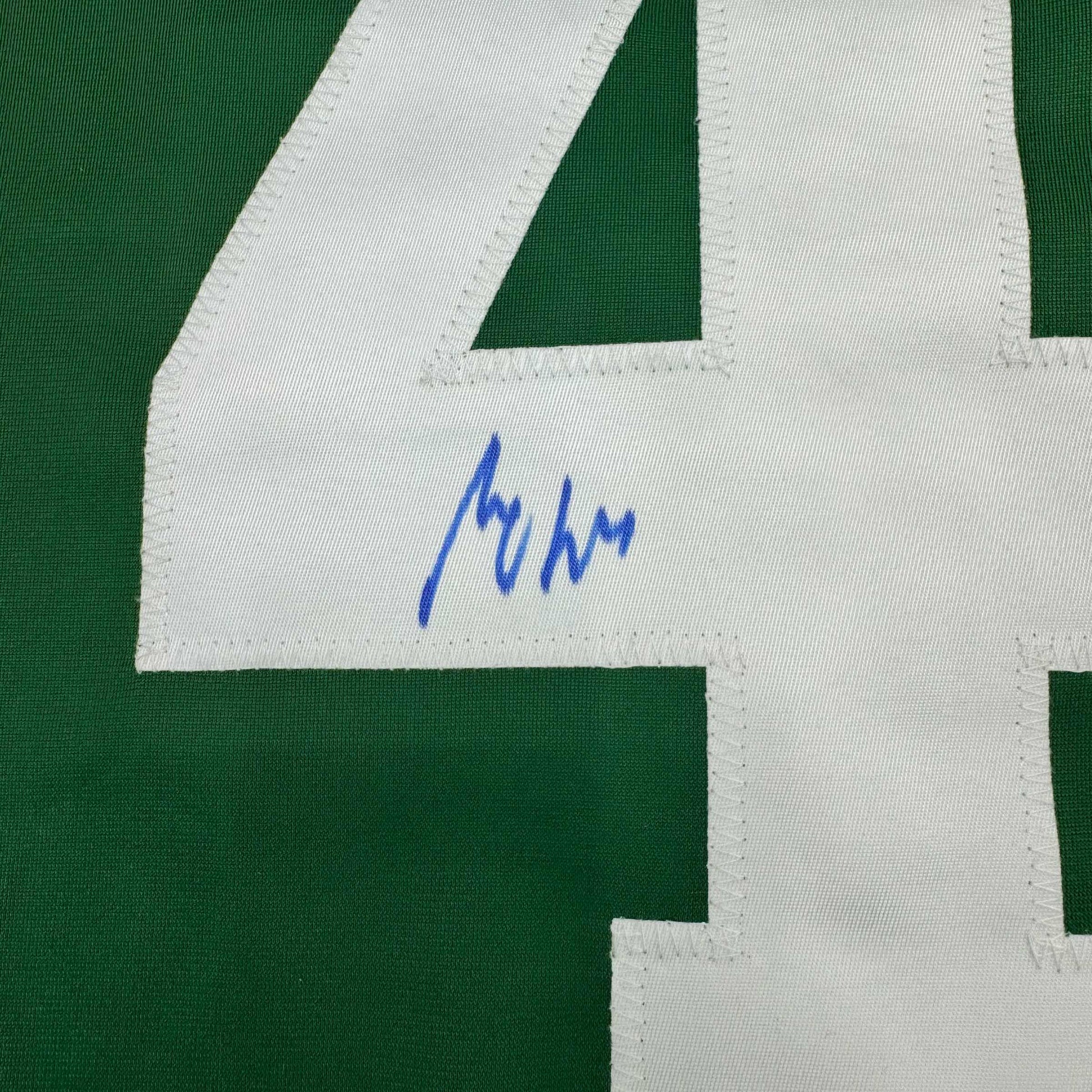 Close-up of blue handwritten signature on white fabric panel of green and white striped hockey jersey.