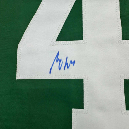 Close-up of blue handwritten signature on white fabric panel of green and white striped hockey jersey.