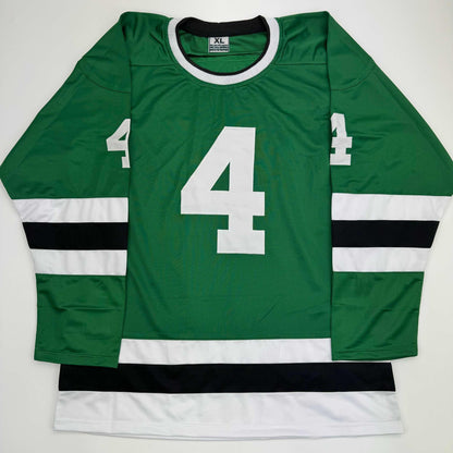Flat lay of green, white, and black hockey jersey with large white number 4 on chest and sleeves.