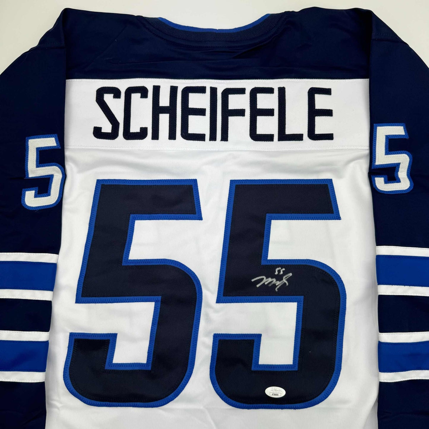 Back view of white hockey jersey with navy sleeves, large navy number 55, blue-outlined numerals, "SCHEIFELE" nameplate, and visible signature on front.