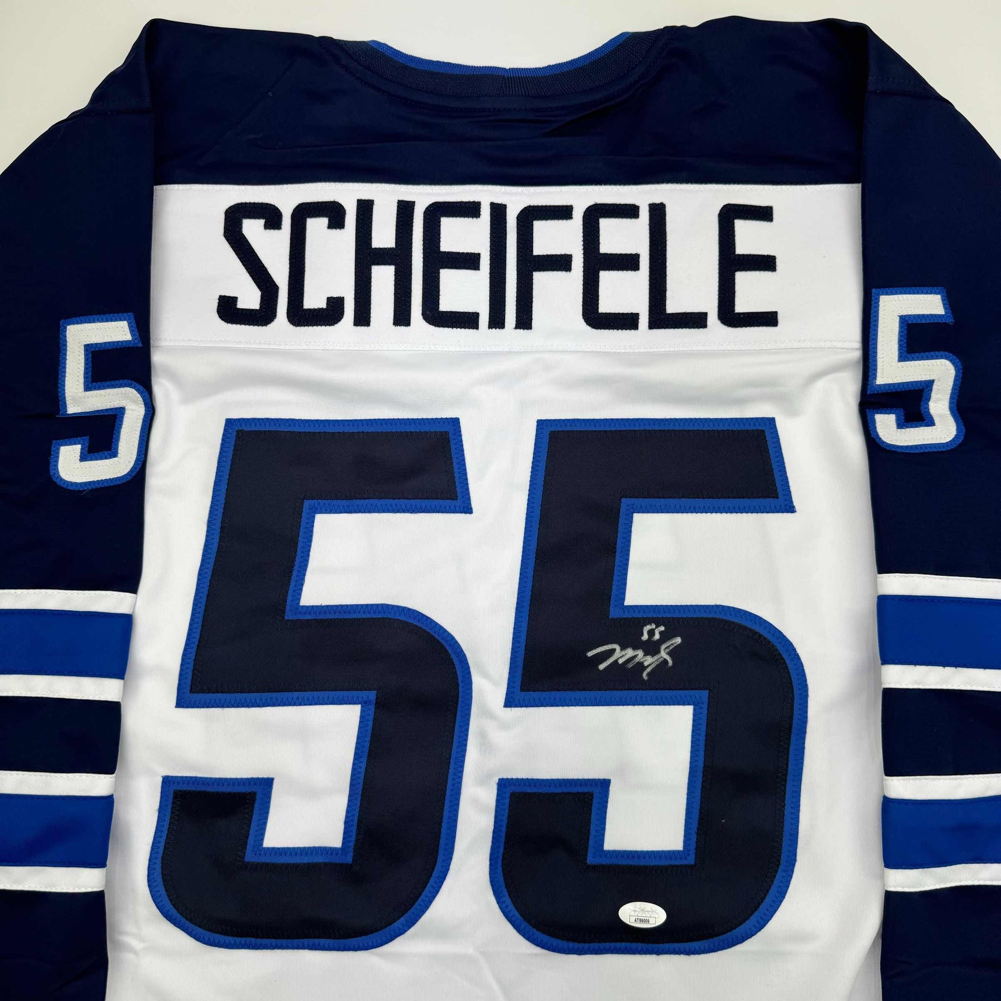Back view of white hockey jersey with navy sleeves, large navy number 55, blue-outlined numerals, "SCHEIFELE" nameplate, and visible signature on front.