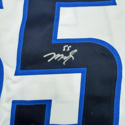Close-up of autographed white hockey jersey with blue and black trim showing Mark Scheifele's signature on dark panel.