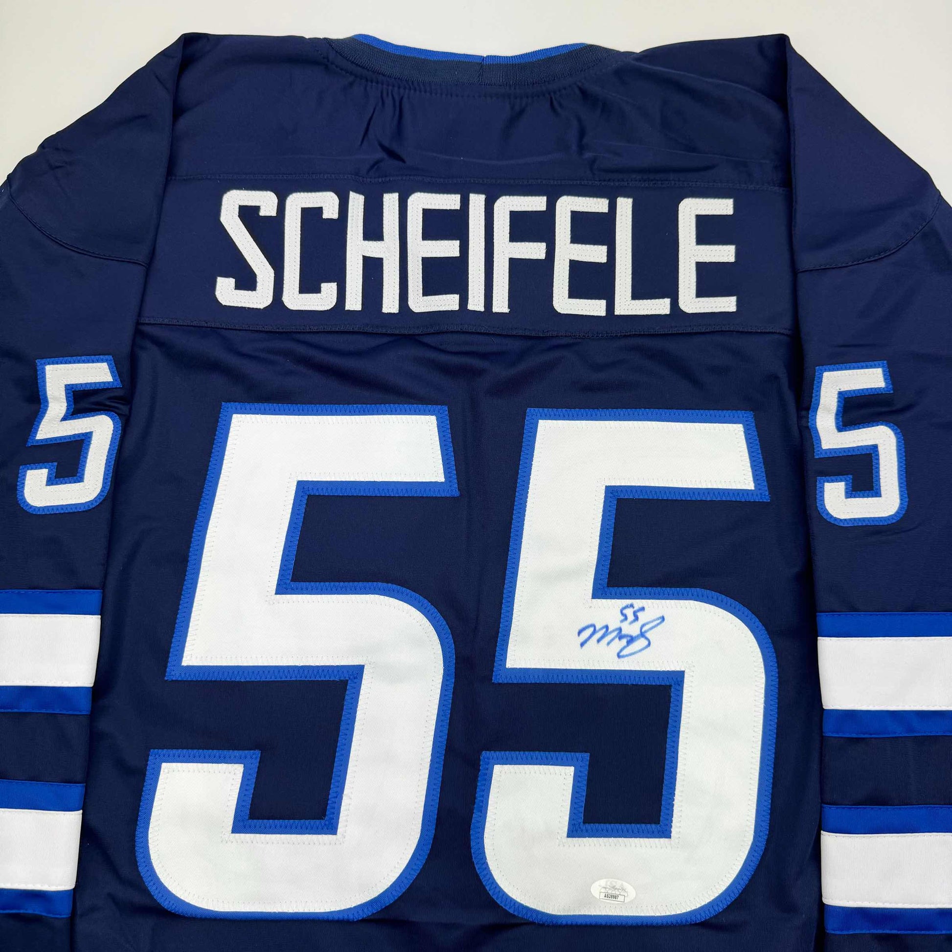 Back view of navy blue hockey jersey with white "SCHEIFELE" nameplate and large white number 55 with blue trim, featuring signature on chest.