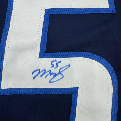 Close-up of blue pen autograph on white curved corner section of navy and blue hockey jersey.