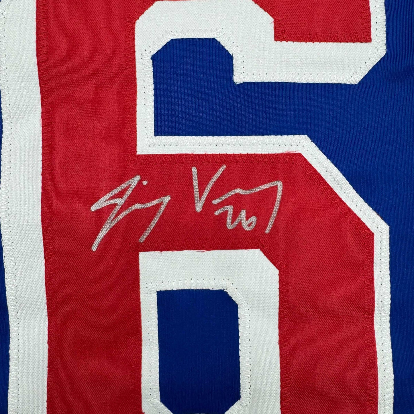 Close-up of autographed red hockey jersey number 5 with white and blue trim showing handwritten signature.