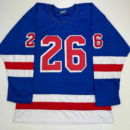 Blue hockey jersey with red and white horizontal stripes, large red number 26 on chest, displayed flat against white background.