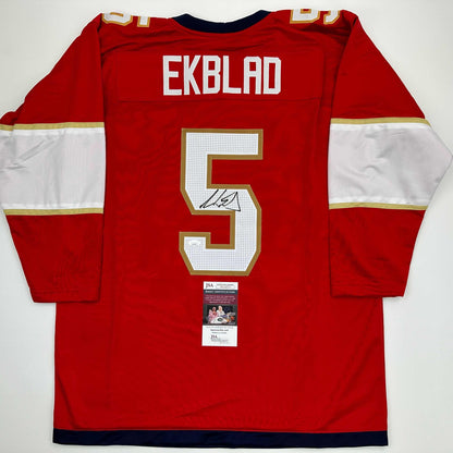 Rear view of red hockey jersey with "EKBLAD" and number 5 in white and gold, JSA authentication certificate visible below neckline.