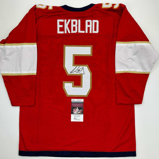 Rear view of red hockey jersey with "EKBLAD" and number 5 in white and gold, JSA authentication certificate visible below neckline.