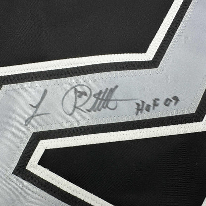 Close-up of signed Luc Robitaille hockey jersey showing autograph on white stripe against black and white striped fabric.