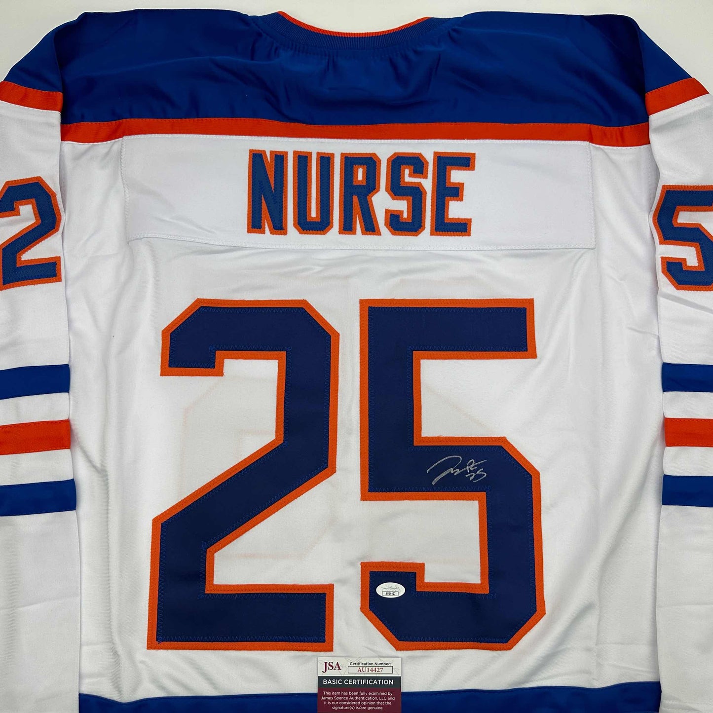 Back view of white hockey jersey with blue and orange trim, "NURSE" and number "25" in blue with orange outline, signed in blue ink, JSA authentication label visible at bottom.