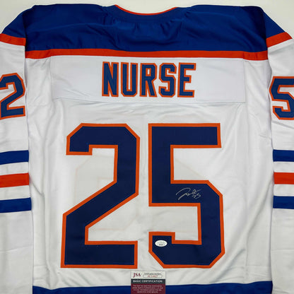 Back view of white hockey jersey with blue and orange trim, "NURSE" and number "25" in blue with orange outline, signed in blue ink, JSA authentication label visible at bottom.