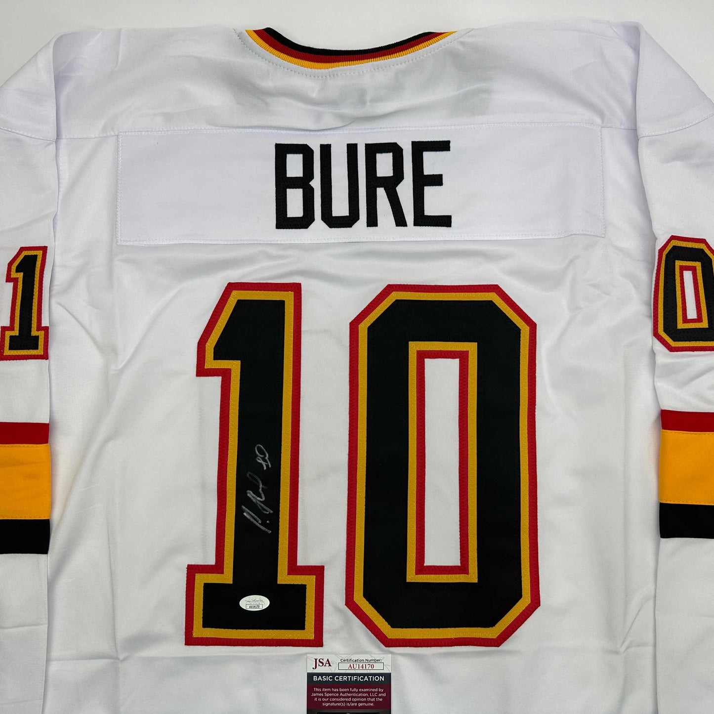 Back view of white hockey jersey displaying "BURE" nameplate and number "10" with red and gold trim, signed in black marker, JSA authentication sticker visible.