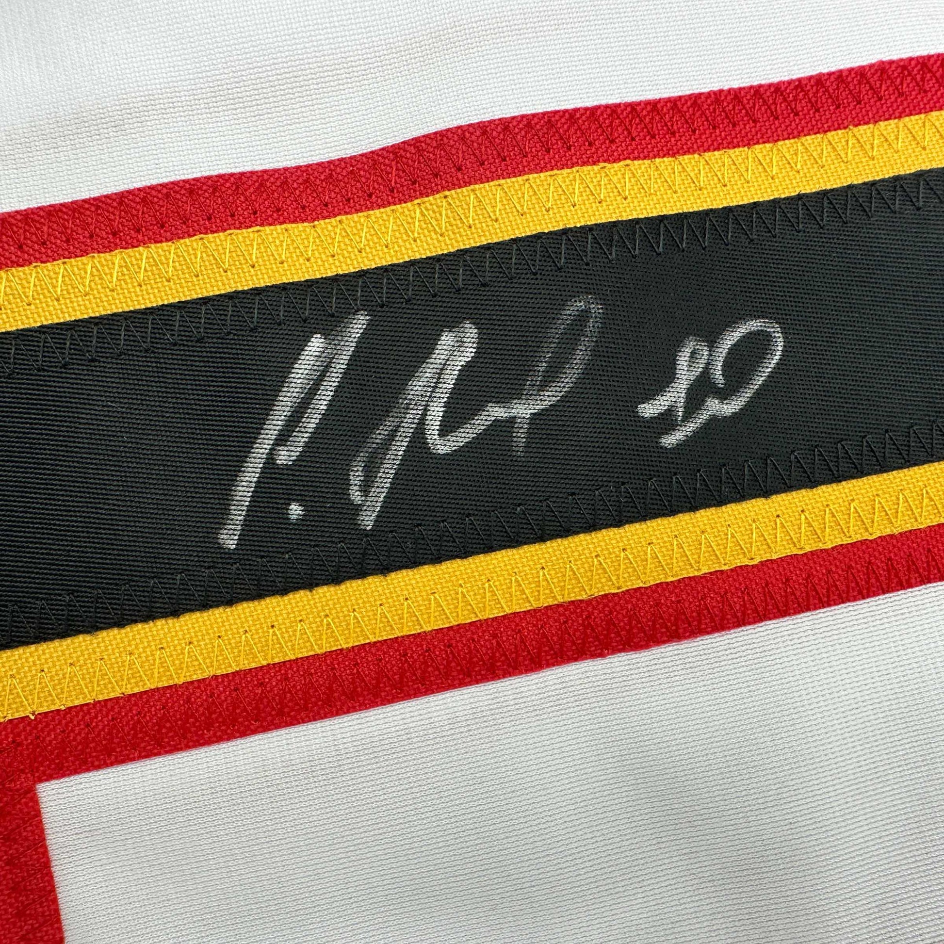 Close-up of black fabric stripe with white handwritten signature on striped hockey jersey with red, yellow, and black bands.