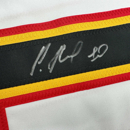 Close-up of black fabric stripe with white handwritten signature on striped hockey jersey with red, yellow, and black bands.