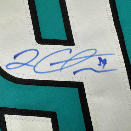 Close-up of blue handwritten signature on white fabric panel of teal and black striped hockey jersey.