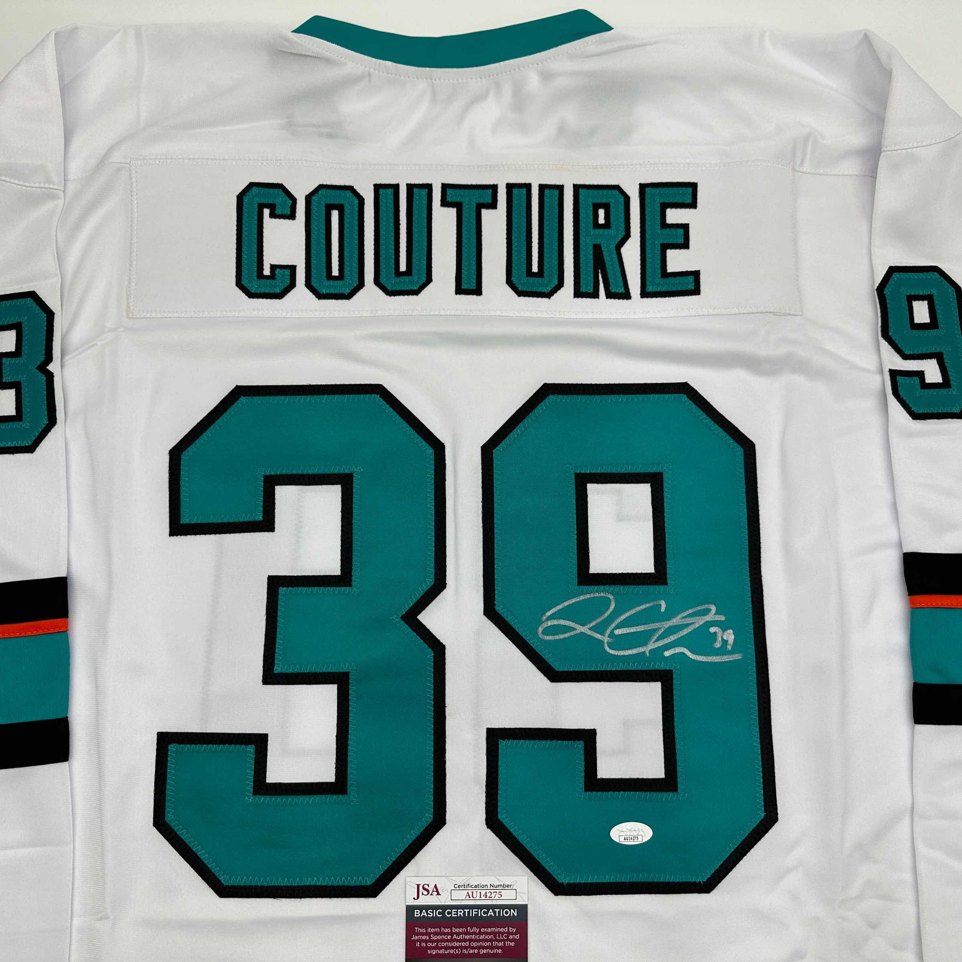 Back view of white hockey jersey with teal and black number 39, "COUTURE" text, and autographed signature with JSA certification label.