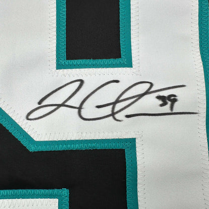 Close-up of handwritten signature on white fabric with turquoise and black striped trim detail.