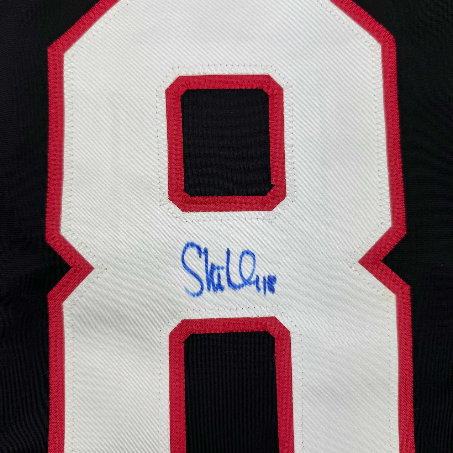 Close-up of white and red hockey jersey back showing number 8 with blue autograph signature below.