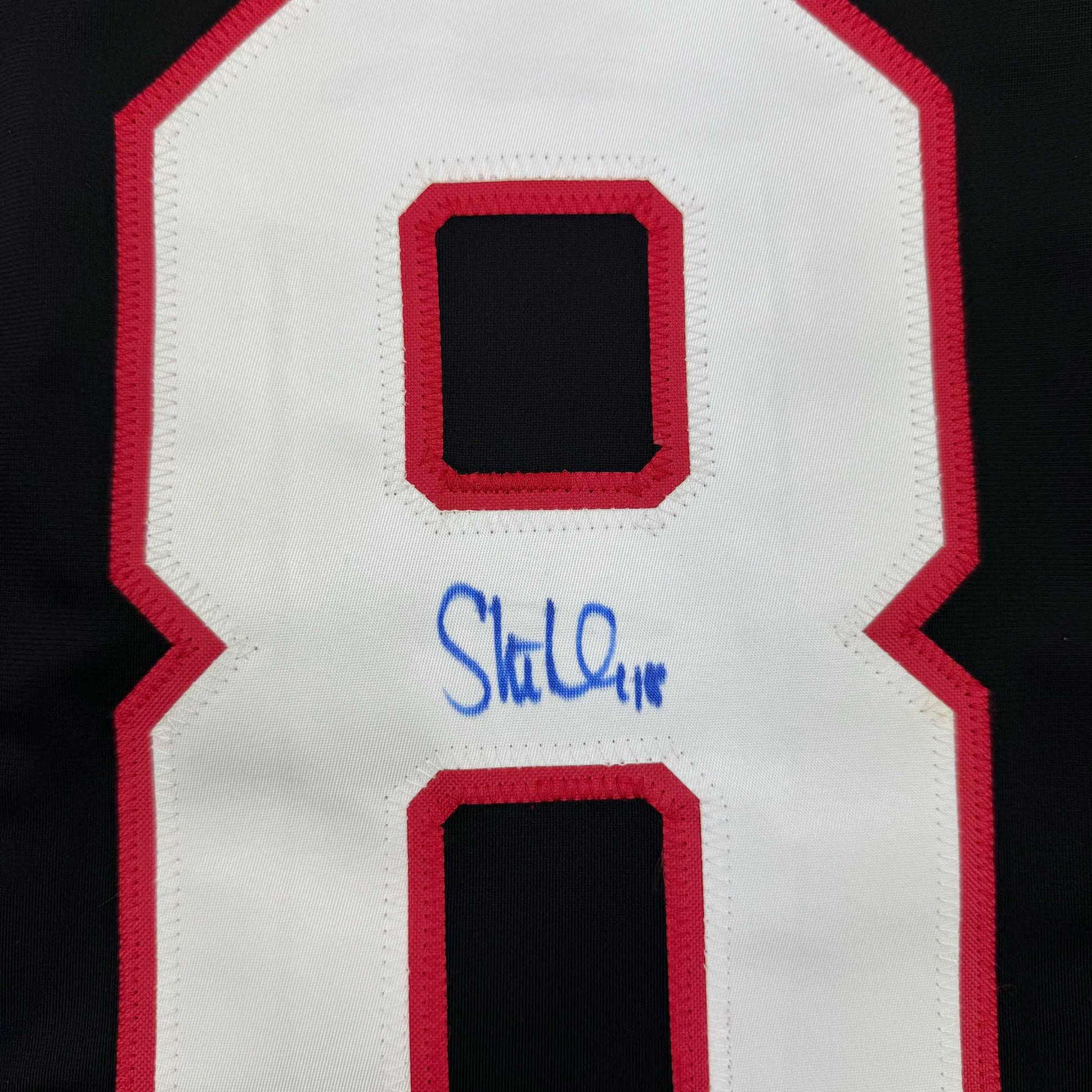 Close-up of red and white hockey jersey back showing number 8 with blue autograph signature below.