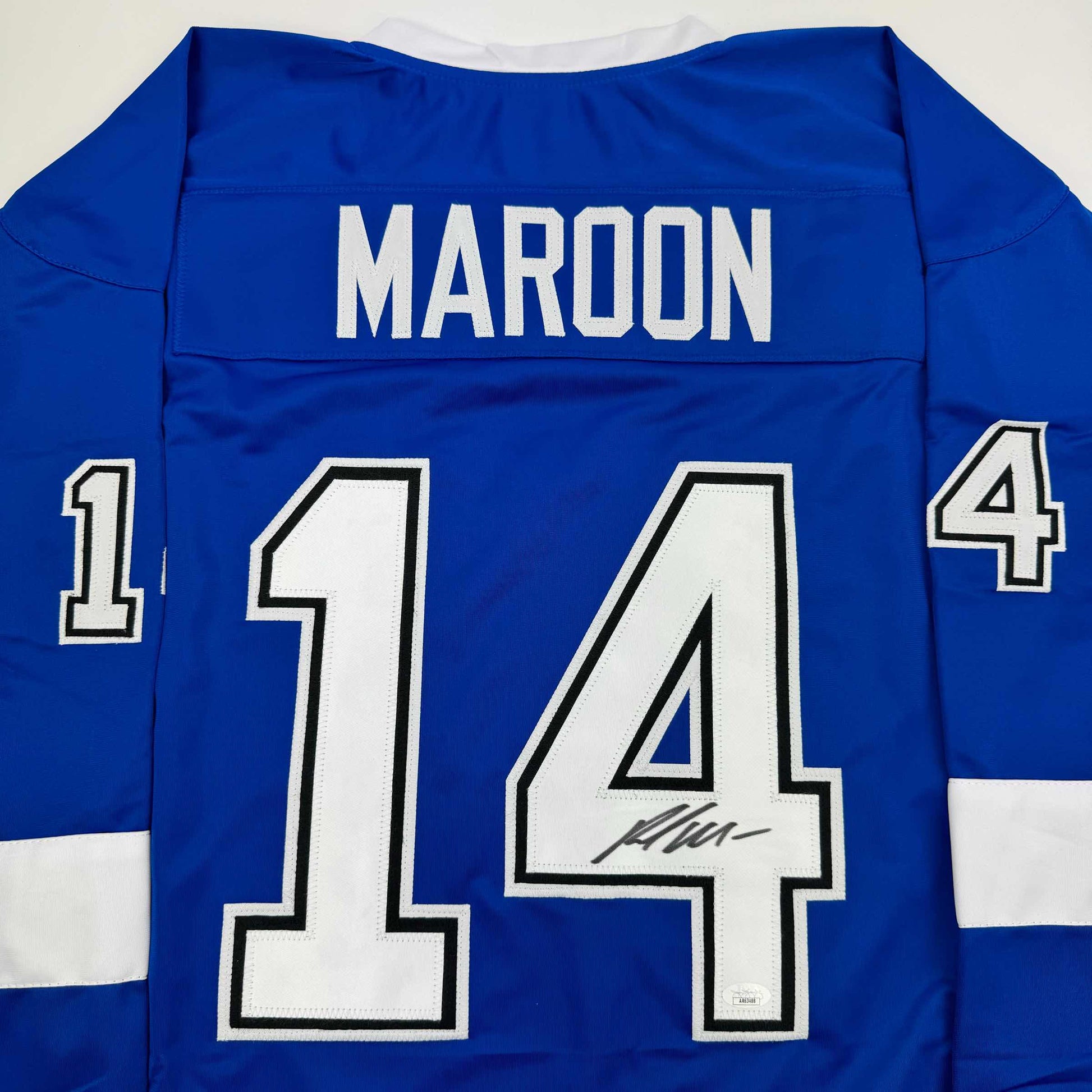 Back view of blue hockey jersey with white "MAROON" nameplate and number 14, featuring an autographed signature on the numbers.