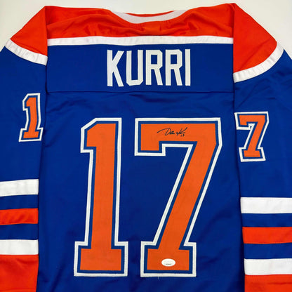 Back view of blue Edmonton Oilers hockey jersey number 17 with "KURRI" nameplate and autographed signature on orange number.