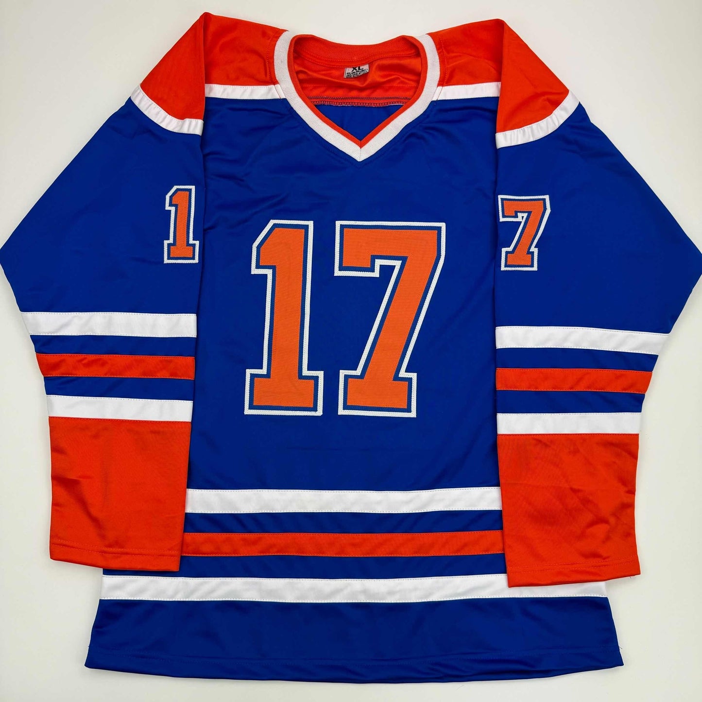 Blue Edmonton Oilers hockey jersey with red and white stripes, orange number 17, displayed flat on white background.