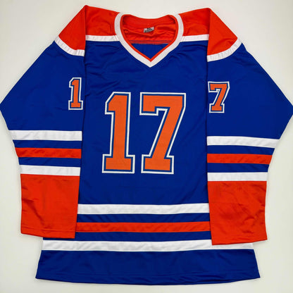 Blue Edmonton Oilers hockey jersey with red and white stripes, orange number 17, displayed flat on white background.