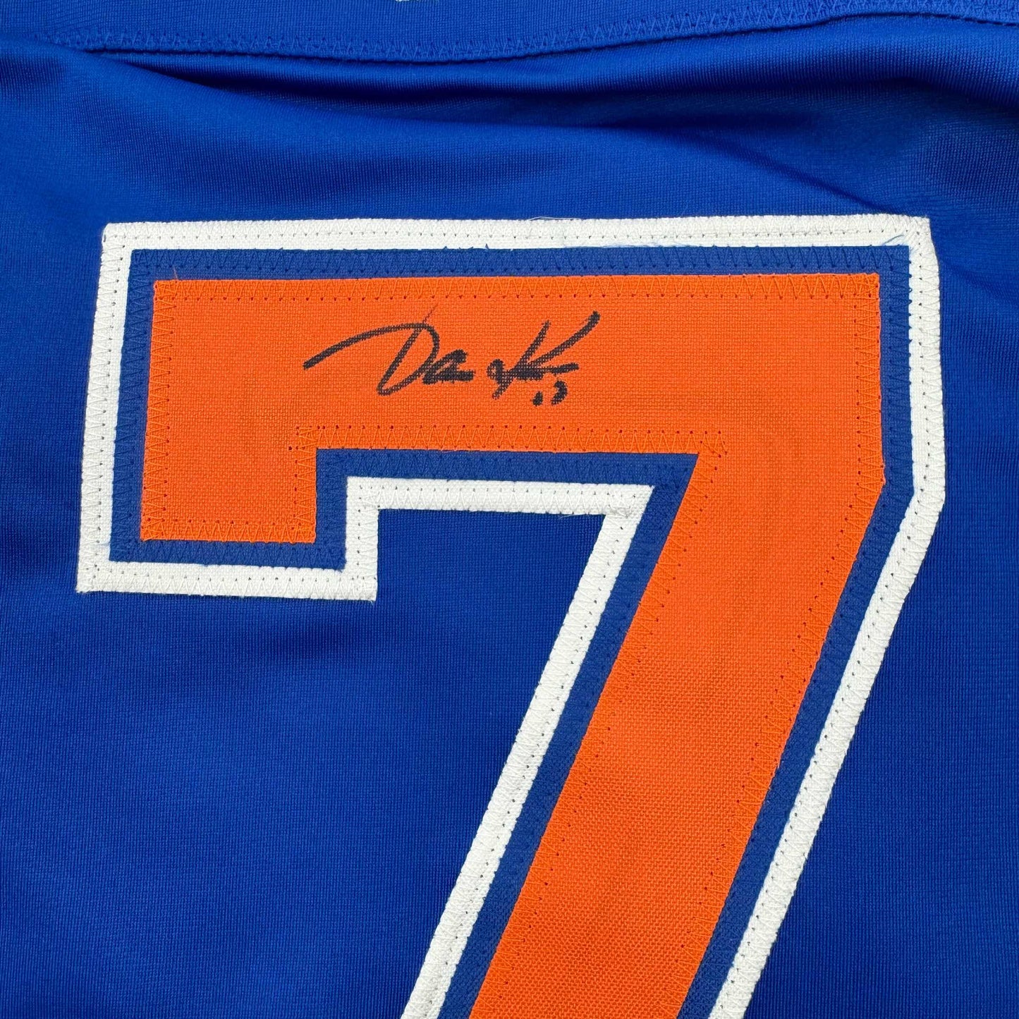 Close-up of signed orange number 7 on blue Edmonton Oilers hockey jersey with white trim.