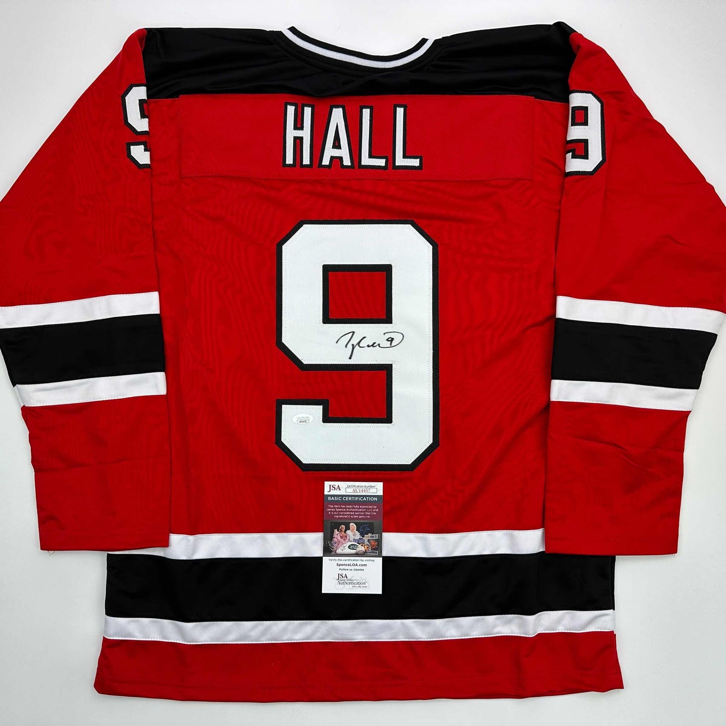 Red hockey jersey with black and white stripes, number 9, "HALL" nameplate, and signature on front, displayed flat with JSA certification label visible at bottom.
