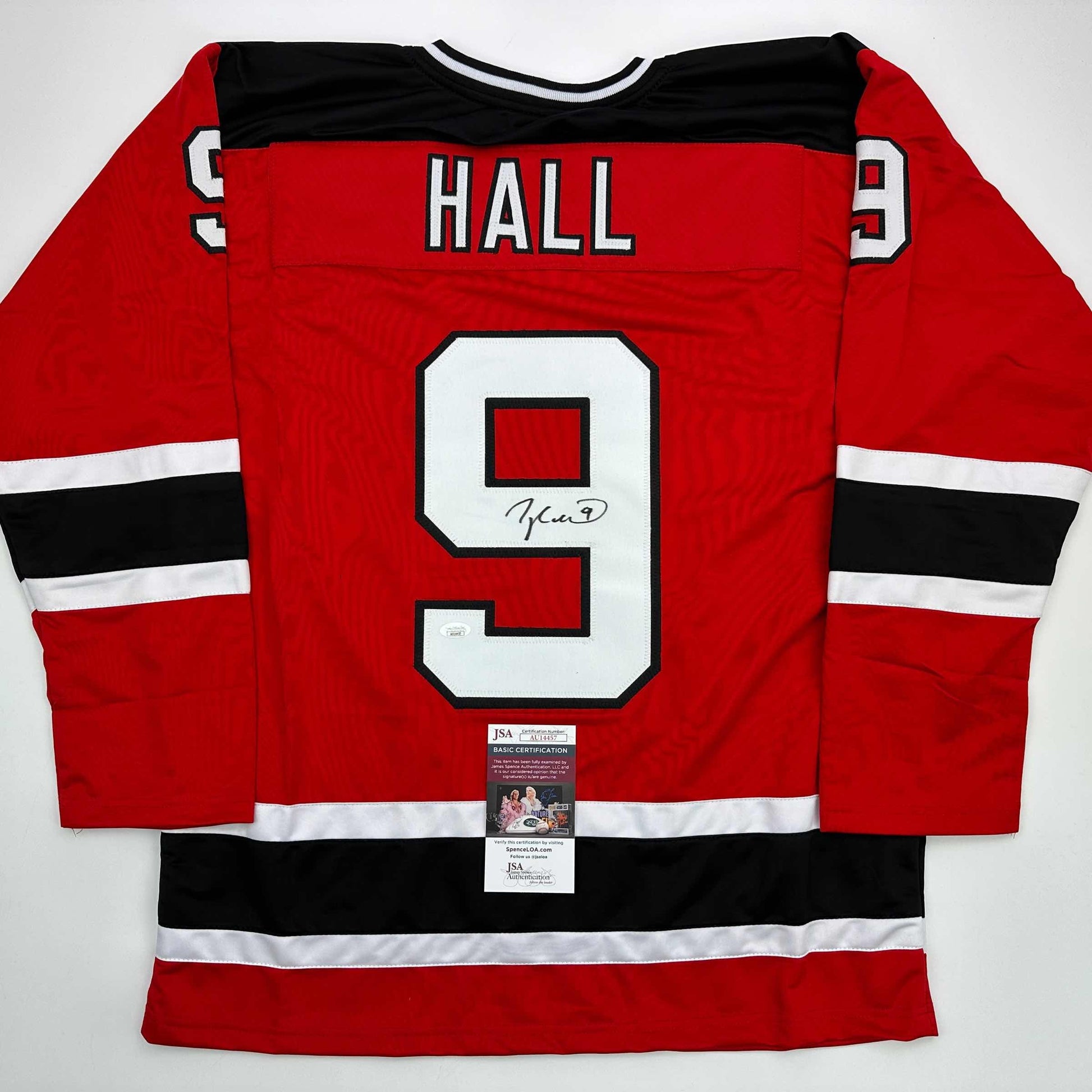 Red hockey jersey with black and white stripes, number 9, "HALL" nameplate, and signature on front, displayed flat with JSA certification label visible at bottom.